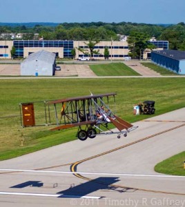 Aerial view of Wright B Flyer's Brown Bird over the runway at Dayton-Wright Brothers Airport with WBF's 1916 Ford Model T Staff Car below.